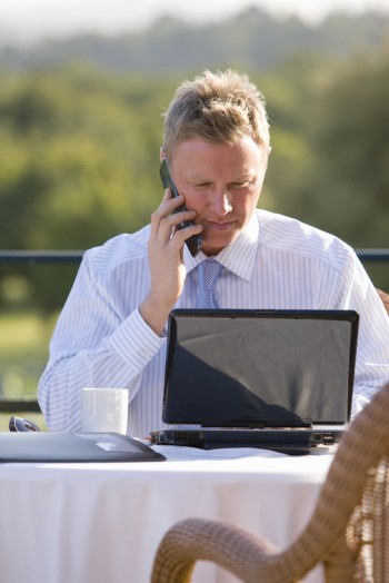 Businessman using cell phone and laptop on cafe patio, Image by © Juice Images/Corbis